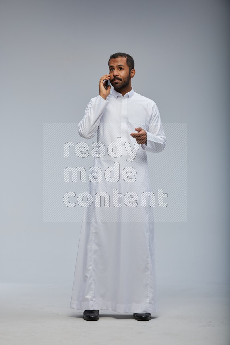 Saudi man wearing Thob standing talking on phone on Gray background