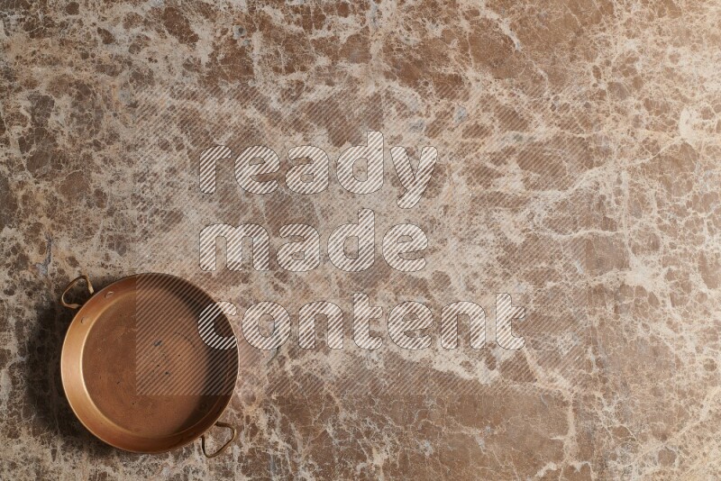 A small copper pan on beige marble background