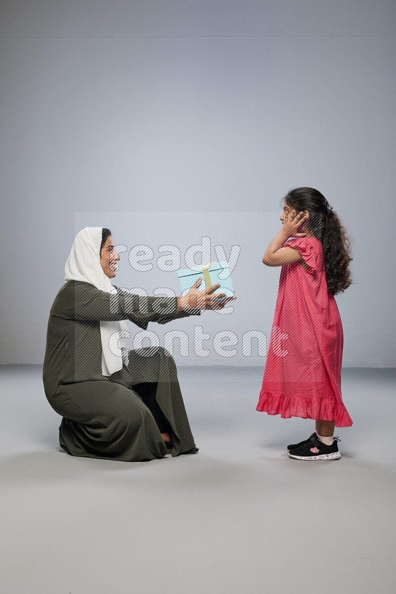 A girl giving a gift to her mother on gray background