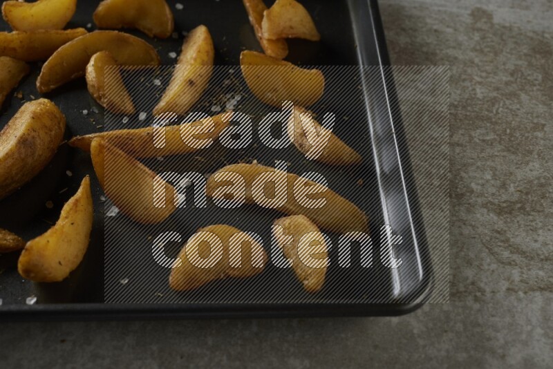 wedges potato in a black stainless steel rectangle tray on grey textured counter top