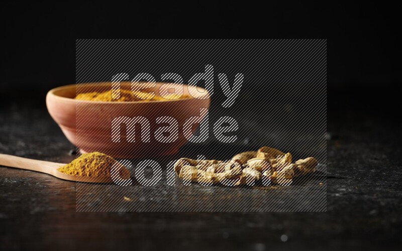 وعاء خشبي وملعقة خشبية ممتلئان ببودرة الكركم مع أصابع الكركم المجففة على خلفية سوداء