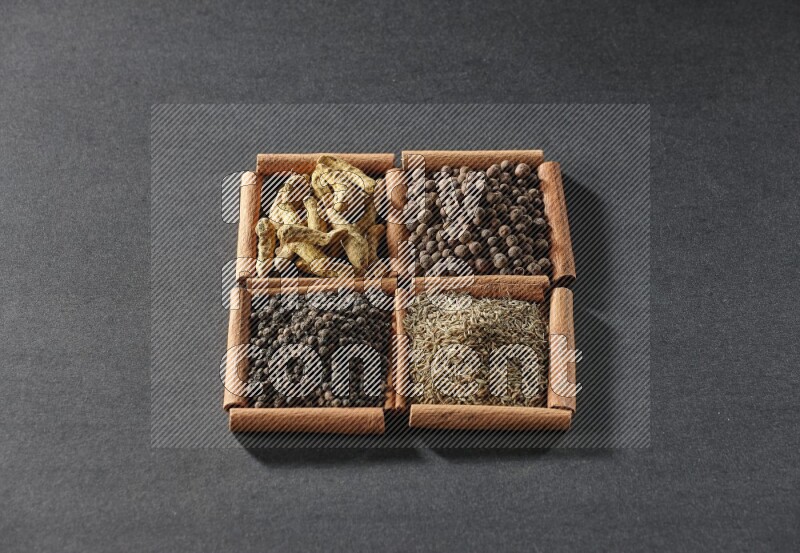 4 مربعات من عيدان القرفة ممتلئة بحبوب الفلفل الأسود والكمون وبهار الفلفل الحلو وأصابع الكركم على أرضية سوداء