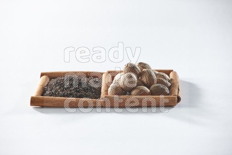 مربعان من أعواد القرفة ممتلئان بالشاي الأسود وجوزة الطيب علي خلفية بيضاء