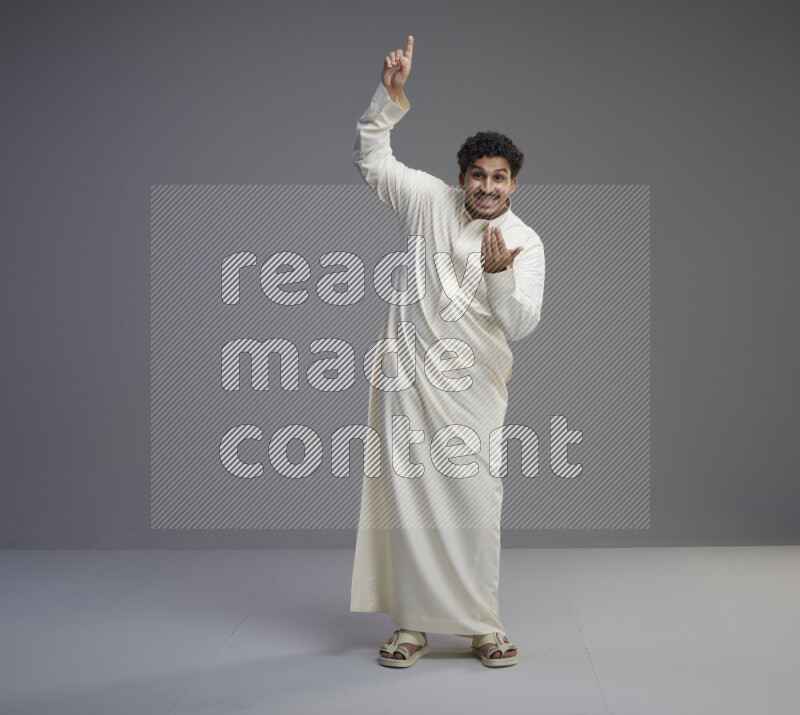 A Saudi man standing wearing thob interacting with the camera on gray background