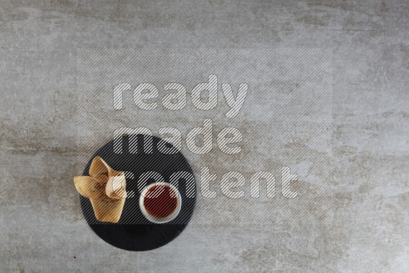 wonton cups with soy sauce ramkin on circle slate on grey textured counter top