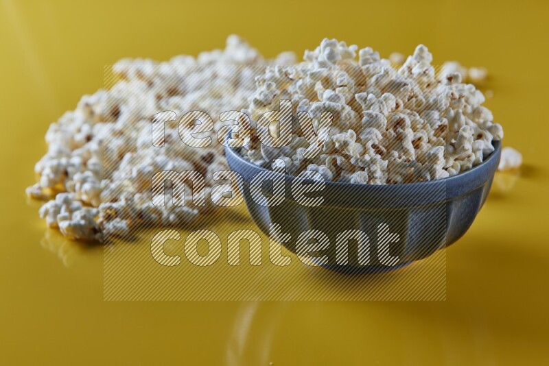 A blue pottery bowl full of popcorn with popcorn beside it on a yellow background in different angles