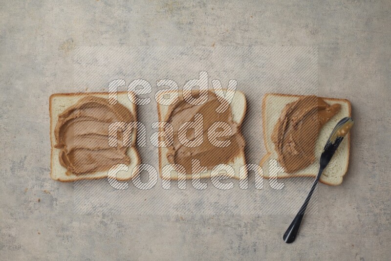 creamy peanut butter on a white toast with a spreading knife on a light blue textured background