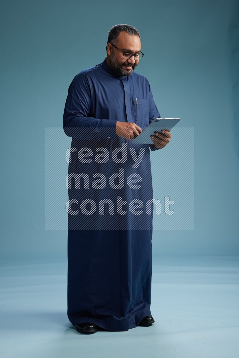 Saudi Man without shimag Standing working on tablet on blue background