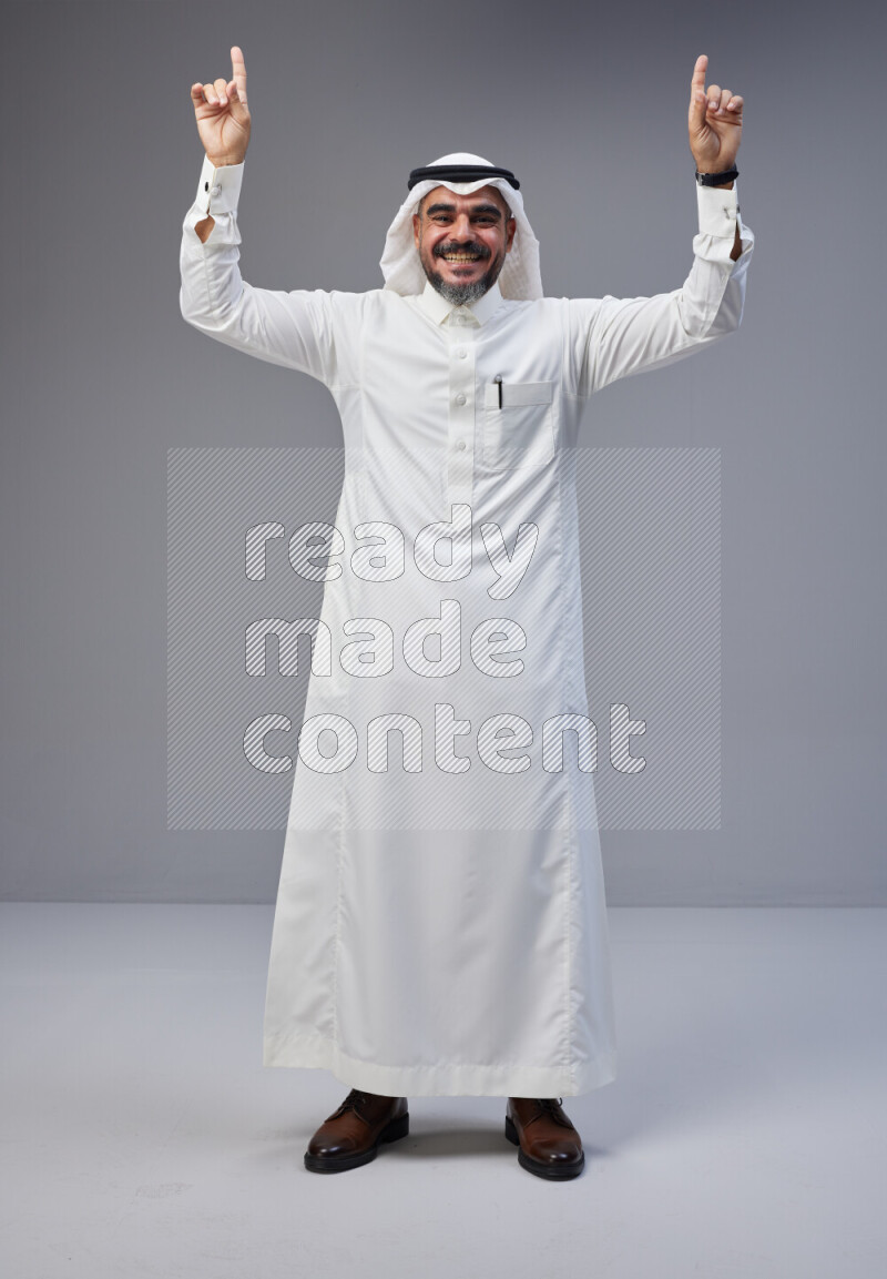 Saudi man Wearing Thob and white Shomag standing interacting with the camera on Gray background