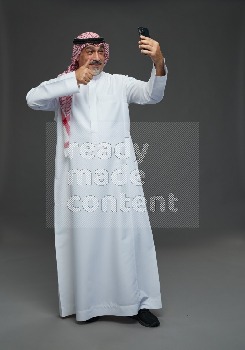 Saudi man with shomag Standing taking selfie on gray background