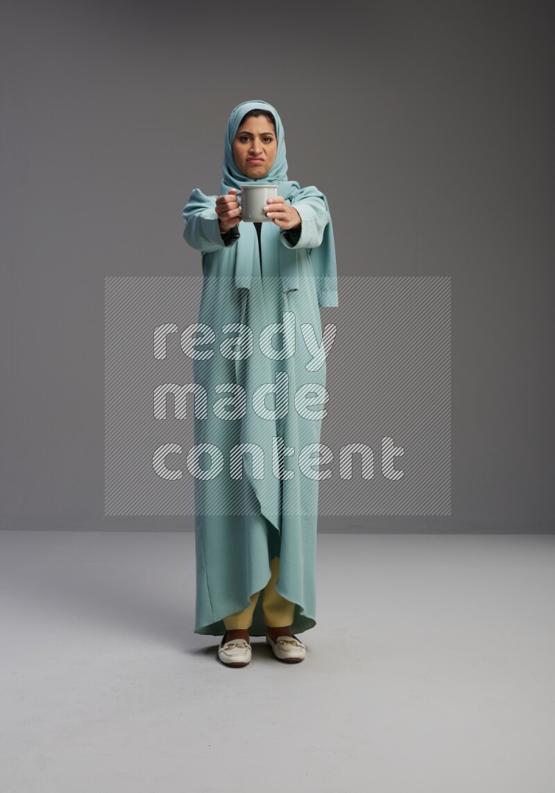 Saudi Woman wearing Abaya standing  holding a mug on Gray background