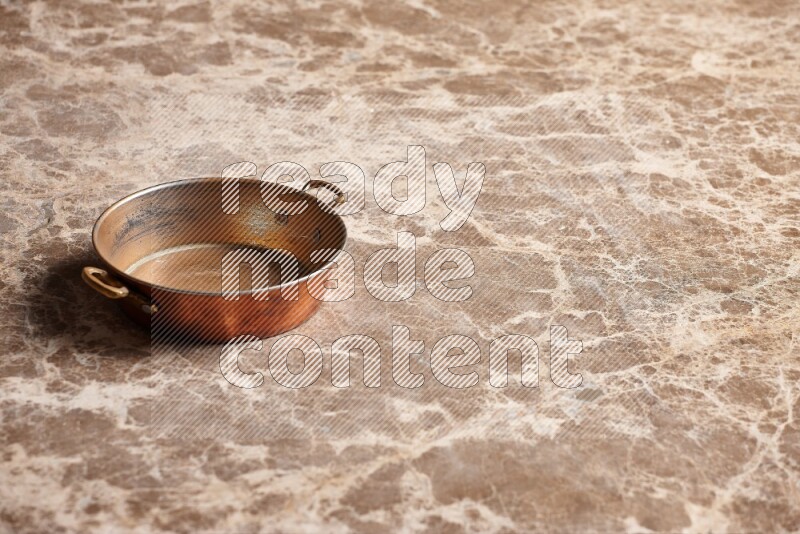 A small copper pan on beige marble background