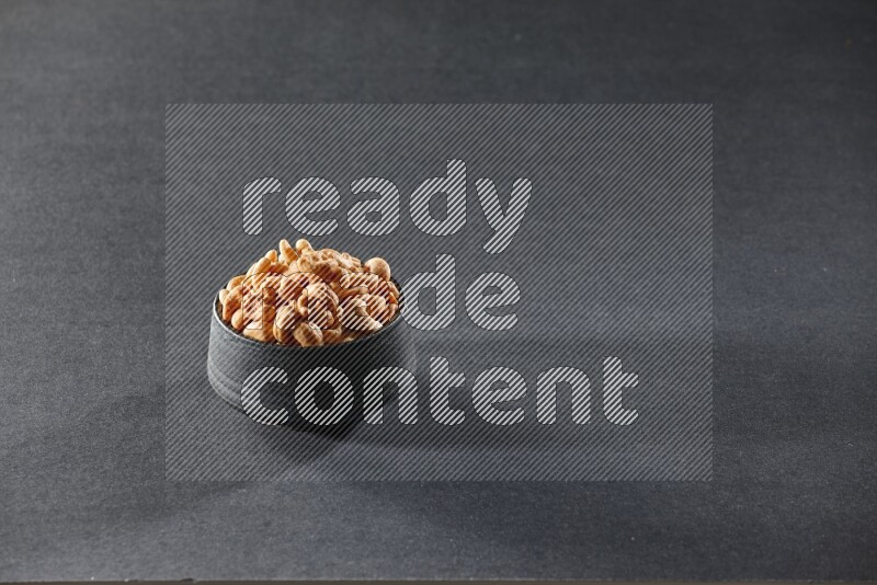 A black pottery bowl full of cashews on a black background in different angles