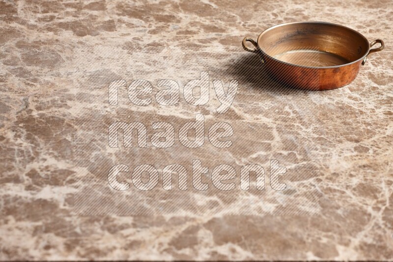 A small copper pan on beige marble background