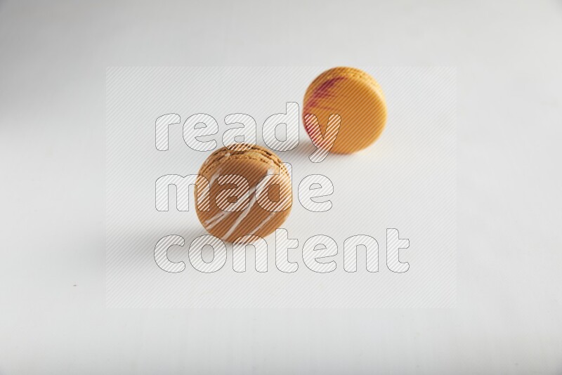 45º Shot of of two assorted Brown Irish Cream, and Orange Exotic macarons on white background