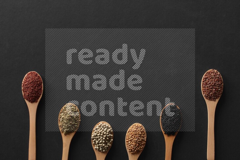 الفلفل الأسود وحبوب الخردل وحبة البركة وحب الرشاد والكمون و حبوب الكتان في معالق خشبية علي خلفية سوداء