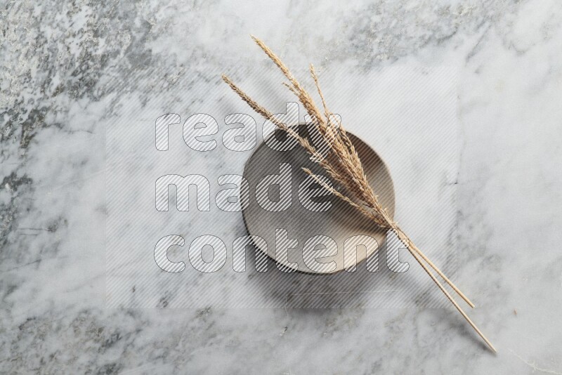 Wheat stalks on multicolored pottery plate on grey marble background