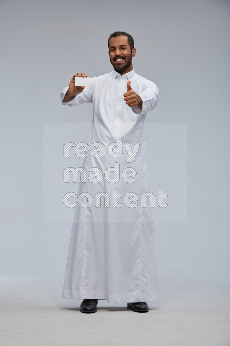 Saudi man wearing Thob standing holding ATM card on Gray background