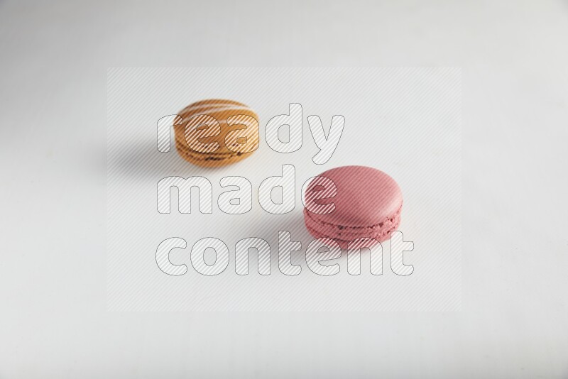 45º Shot of of two assorted Brown Irish Cream, and Pink Raspberry macarons on white background