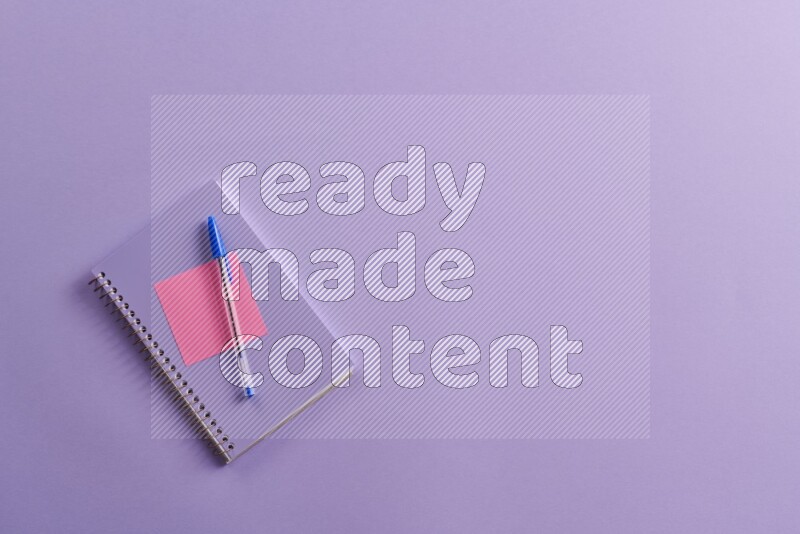 A purple notebook with different school supplies on purple background