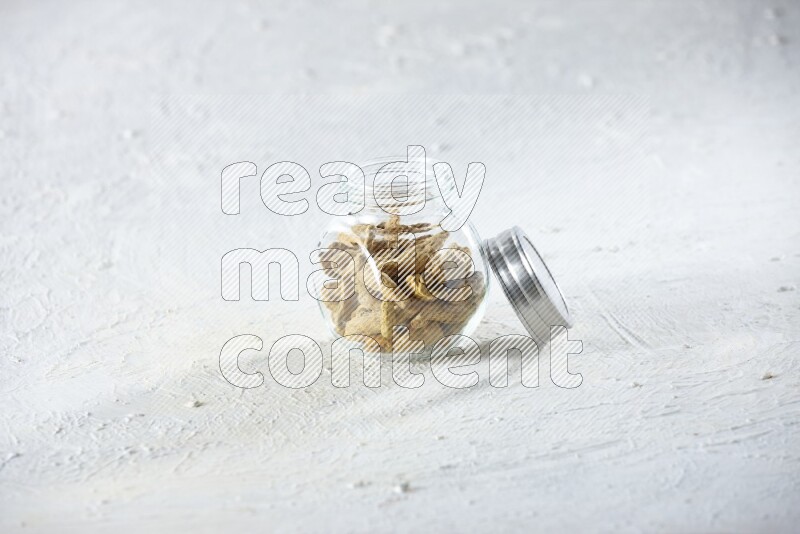 A glass spice jar full of dried turmeric whole fingers on a textured white flooring