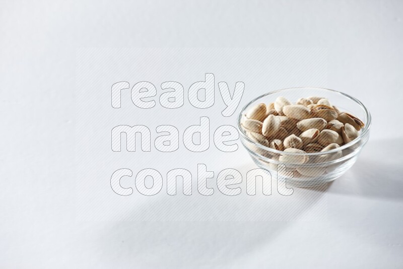 A glass bowl full of pistachios on a white background in different angles