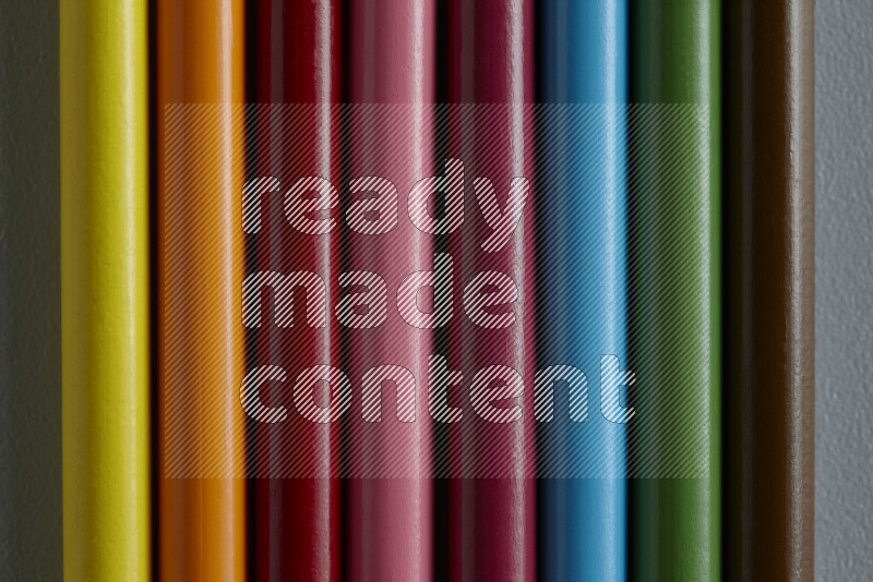 A collection of colored pencils arranged showcasing a gradient of different hues on grey background
