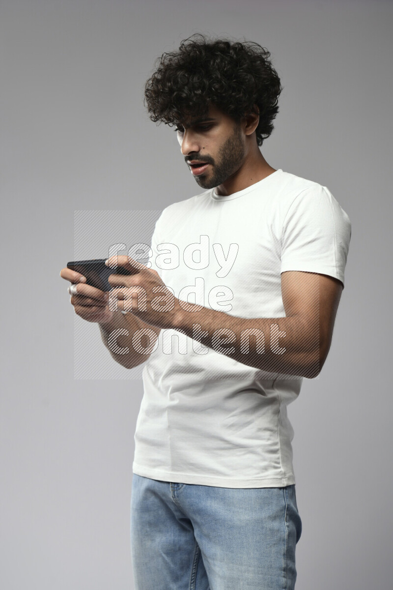 A man wearing casual standing and gaming on the phone on white background