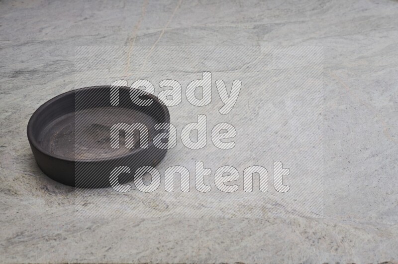 A black pottery oven bowl on grey marble background