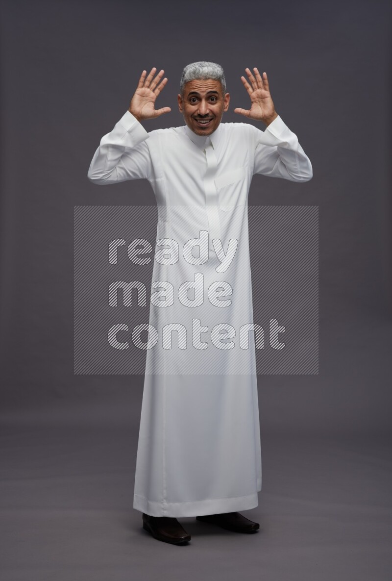 Saudi man wearing thob standing hands behind head on gray background