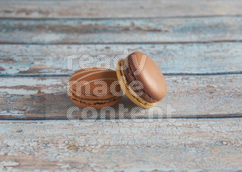 45º Shot of of two assorted Brown Irish Cream, and Yellow, and Brown Chai Latte macarons  on light blue background