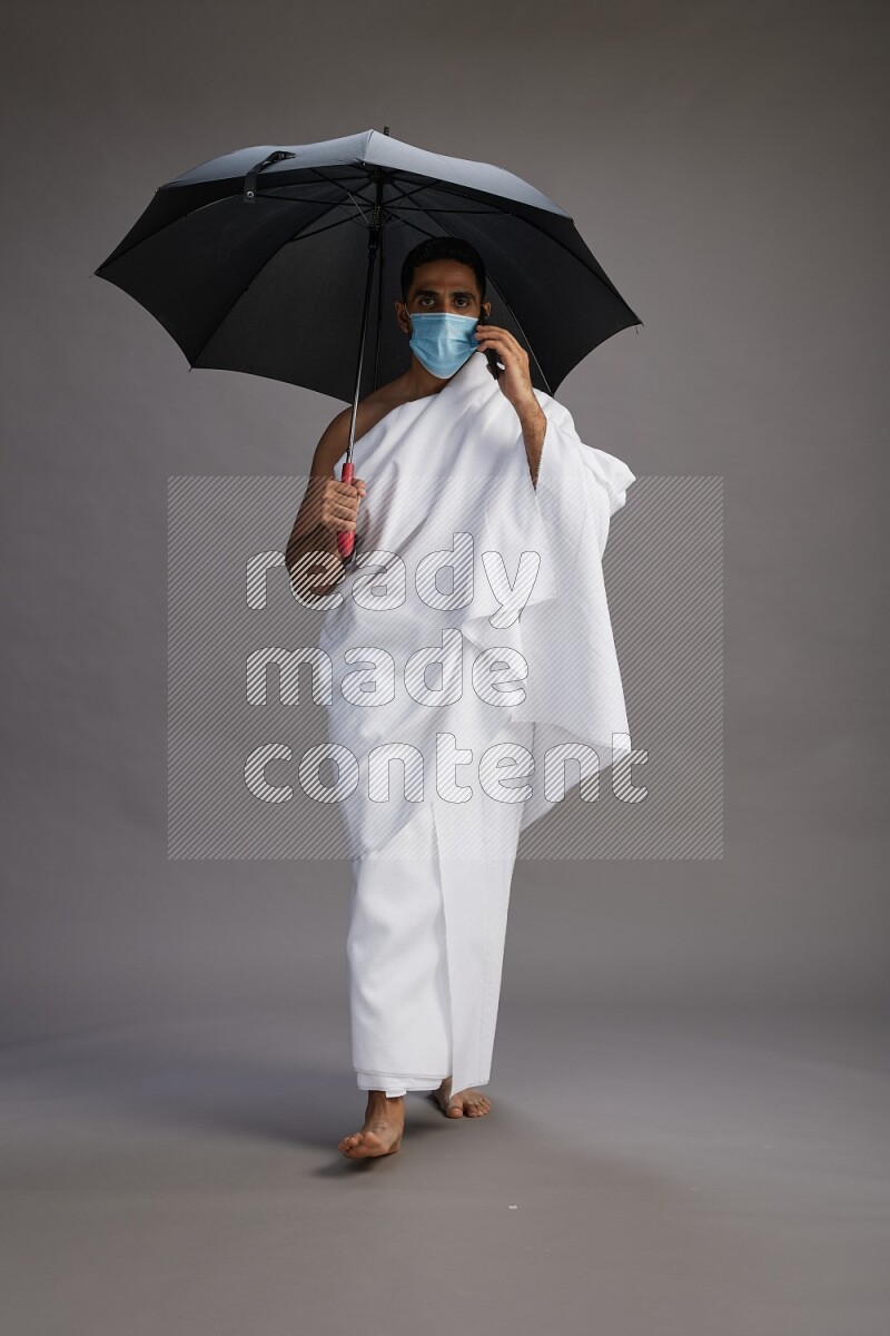 A man wearing Ehram and mask Standing holding umbrella on gray background on gray background