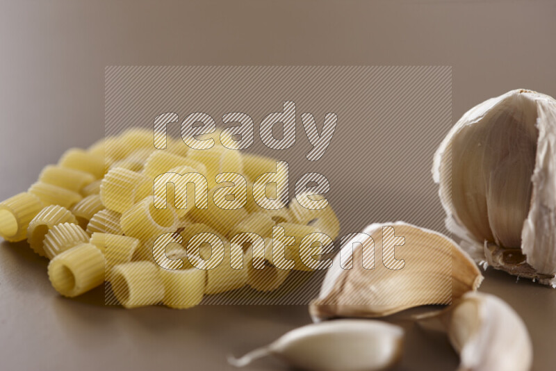 Raw pasta with different ingredients such as cherry tomatoes, garlic, onions, red chilis, black pepper, white pepper, bay laurel leaves, rosemary and cardamom on beige background