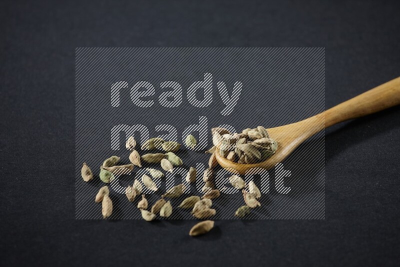 A wooden spoon full of cardamom on black flooring