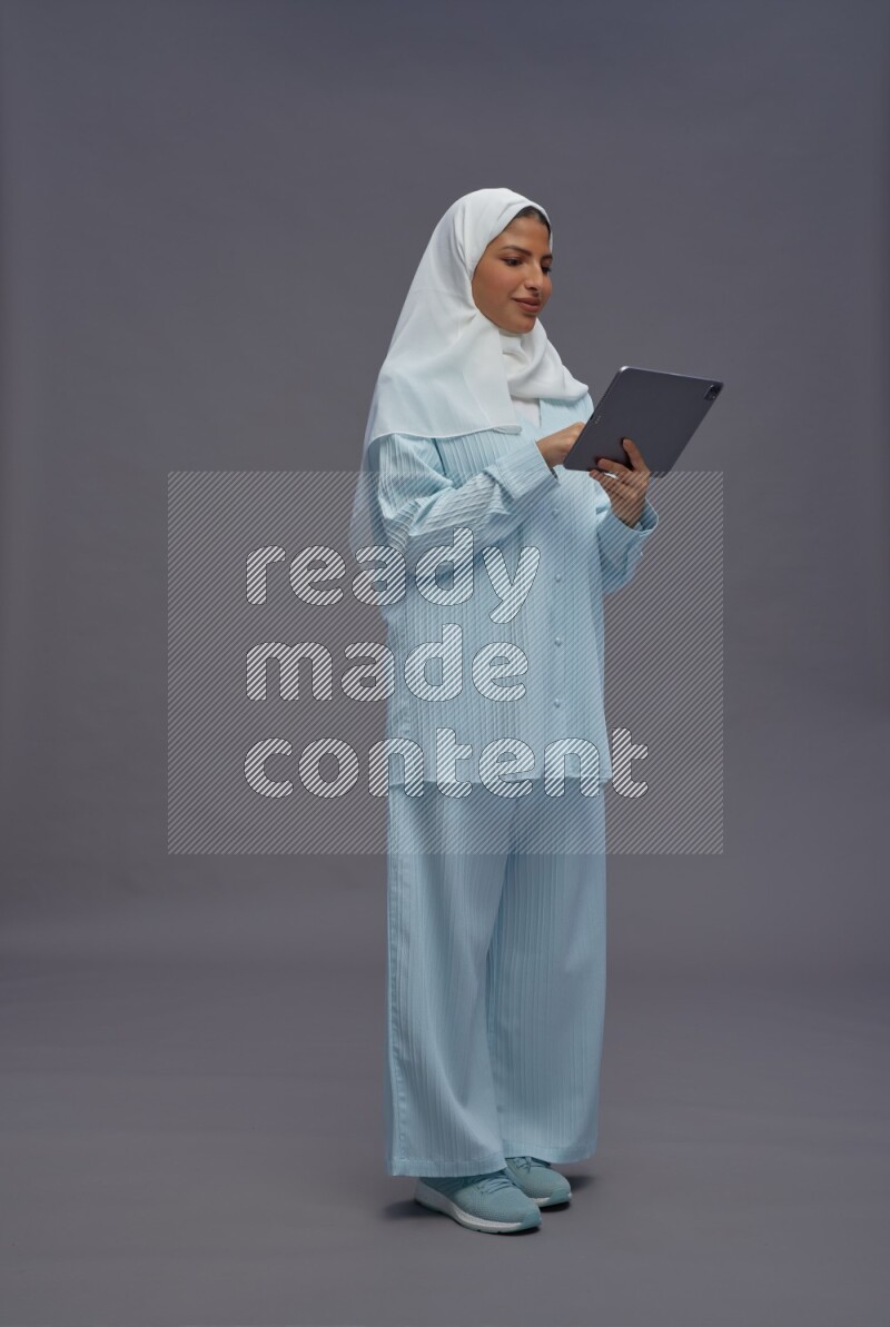 Saudi woman wearing hijab clothes standing working on tablet on gray background