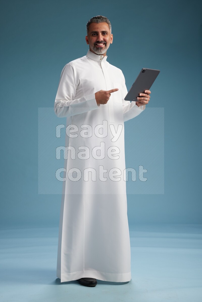 Saudi man waring thob with tablet on blue background