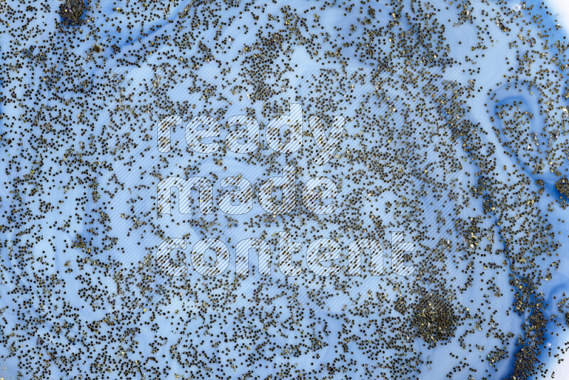 A close-up of sparkling gold glitter scattered on swirling blue background