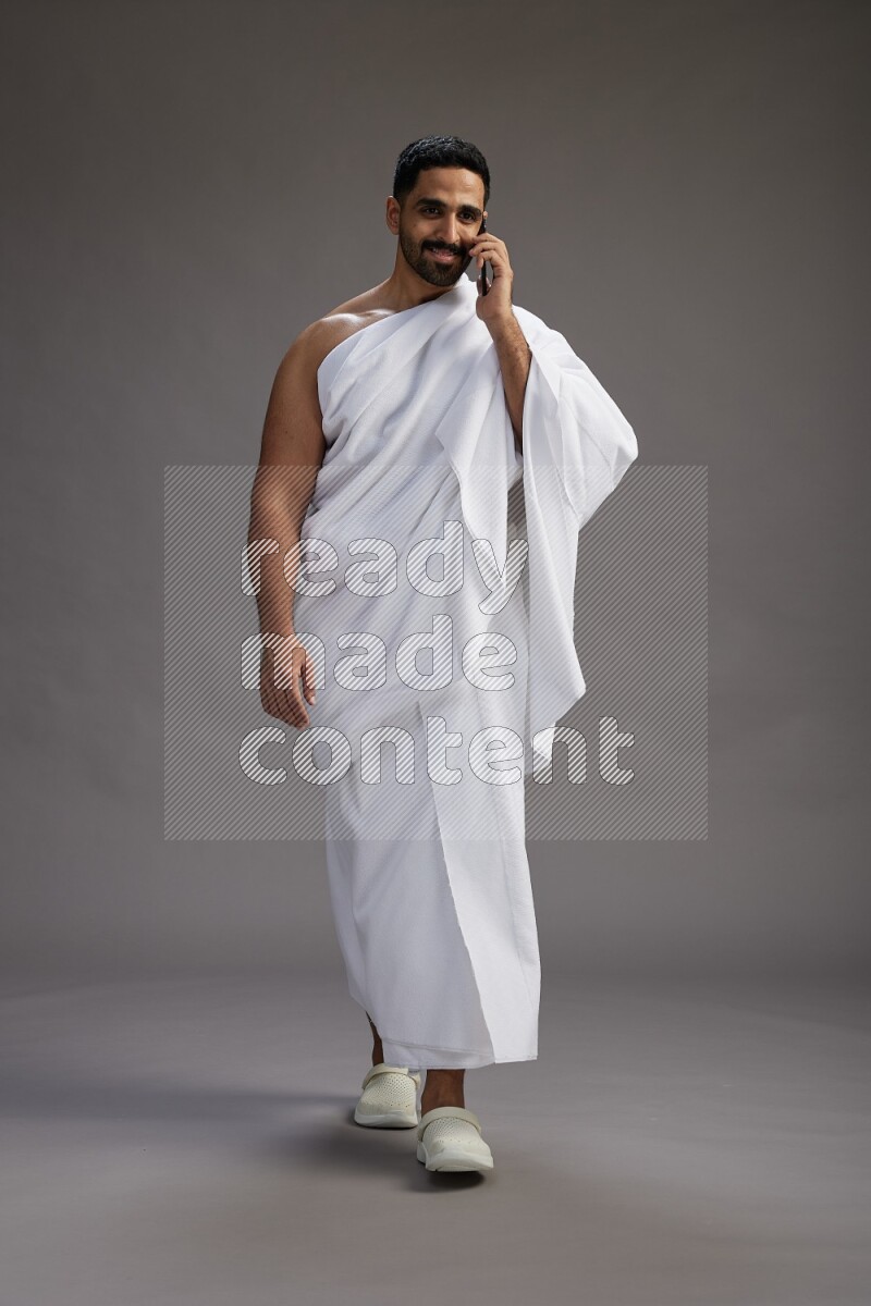 A man wearing Ehram Standing talking on phone on gray background