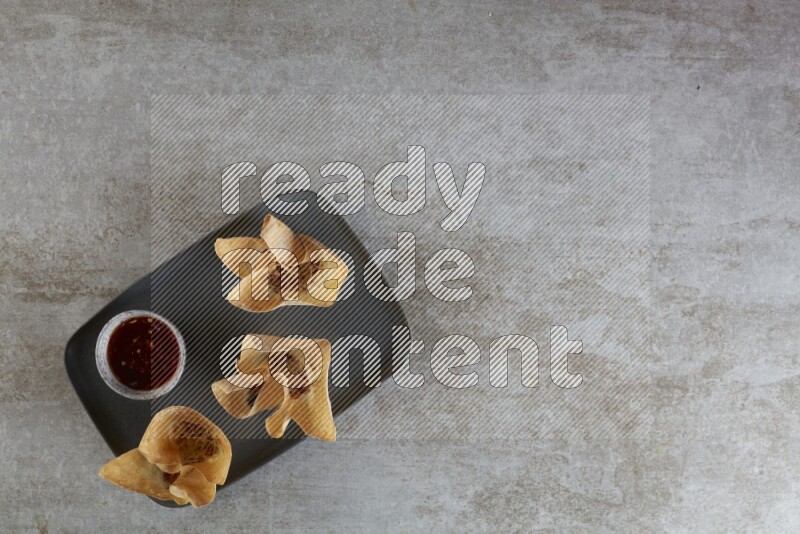 wonton cups with soy sauce ramkin on rectangle dark grey ceramic plate on grey textured counter top
