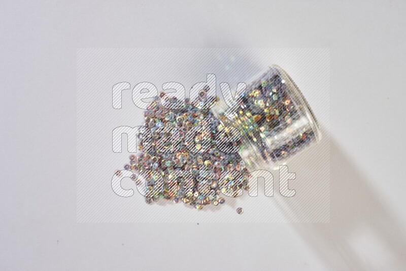 Colored flat sequins in a glass jar on grey background