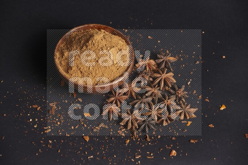 Star Anise powder in a wooden bowl with star anise beside it on a black background