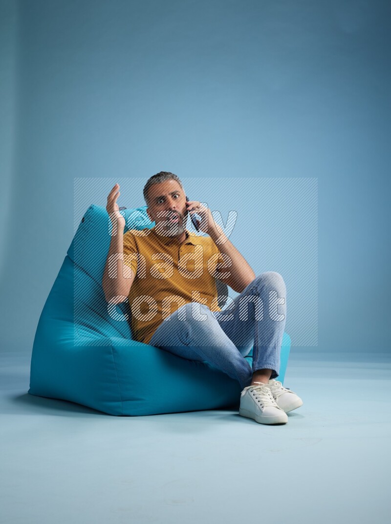 A man sitting on a blue beanbag and talking on the phone