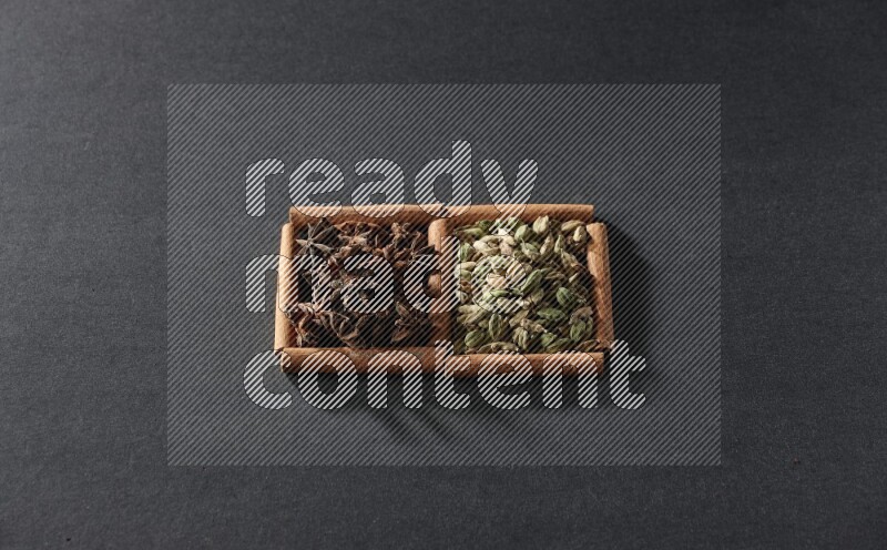 مربعان من أعواد القرفة ممتلئان بحبوب الهيل واليانسون النجمي علي خلفية سوداء