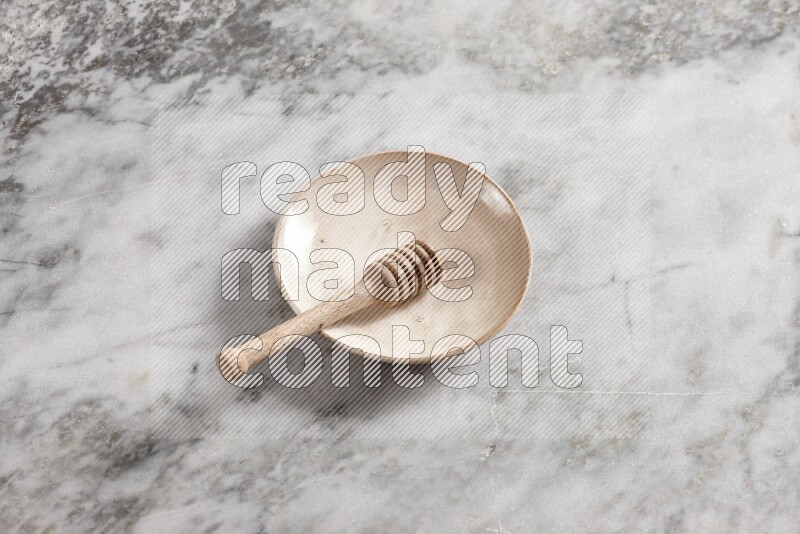 Beige pottery plate with wooden honey dipper in it on grey marble background