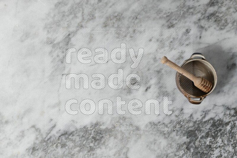 وعاء فخاري متعدد الألوان مع ملعقة عسل خشبية بداخله على خلفية من الرخام الرمادي