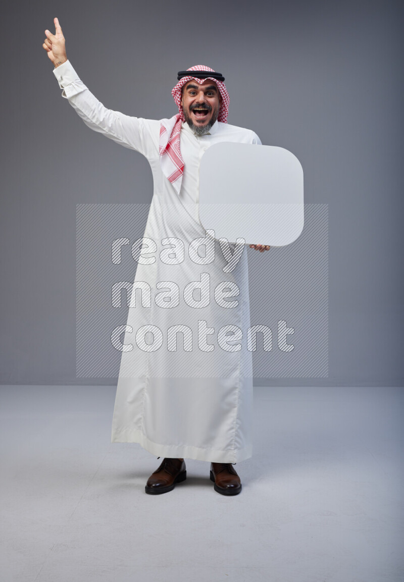 Saudi man Wearing Thob and red Shomag standing holding social media sign on Gray background