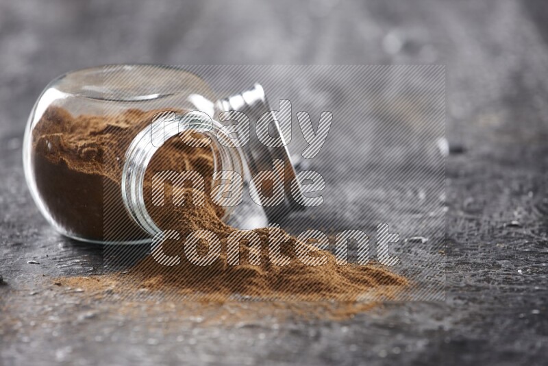 Flipped herbal glass jar full of cinnamon powder on textured black background