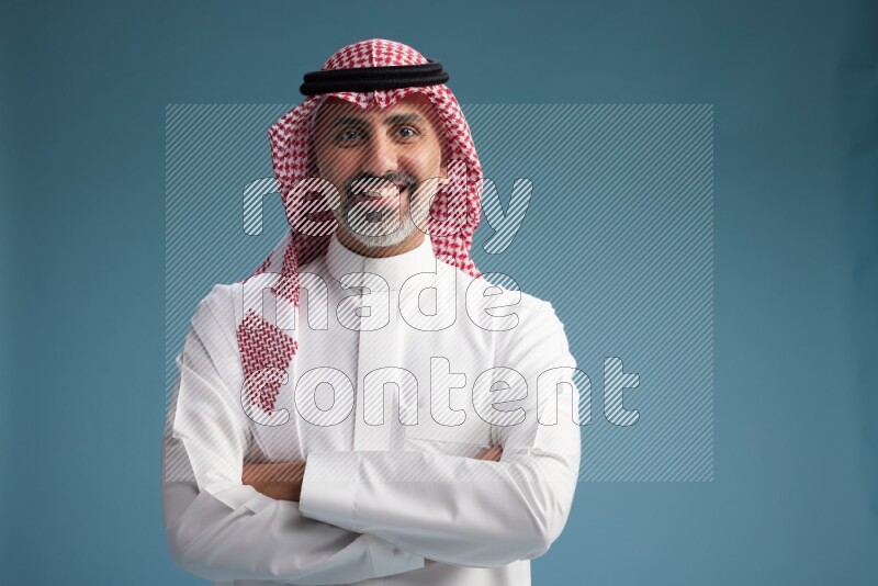Saudi man wearing thob and shomagh posing to the camera on blue background
