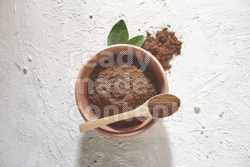 A wooden bowl and a wooden spoon full of cloves powder on a textured white flooring