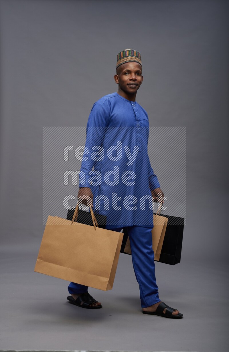 Man wearing Nigerian outfit standing holding shopping bag on gray background